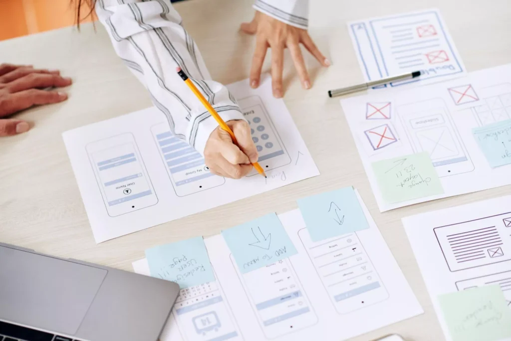 Mobile app UX planning with paper wireframes, sticky notes, and screen sketches during the design phase